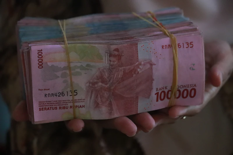 Tangan memegang setumpuk uang kertas Rupiah